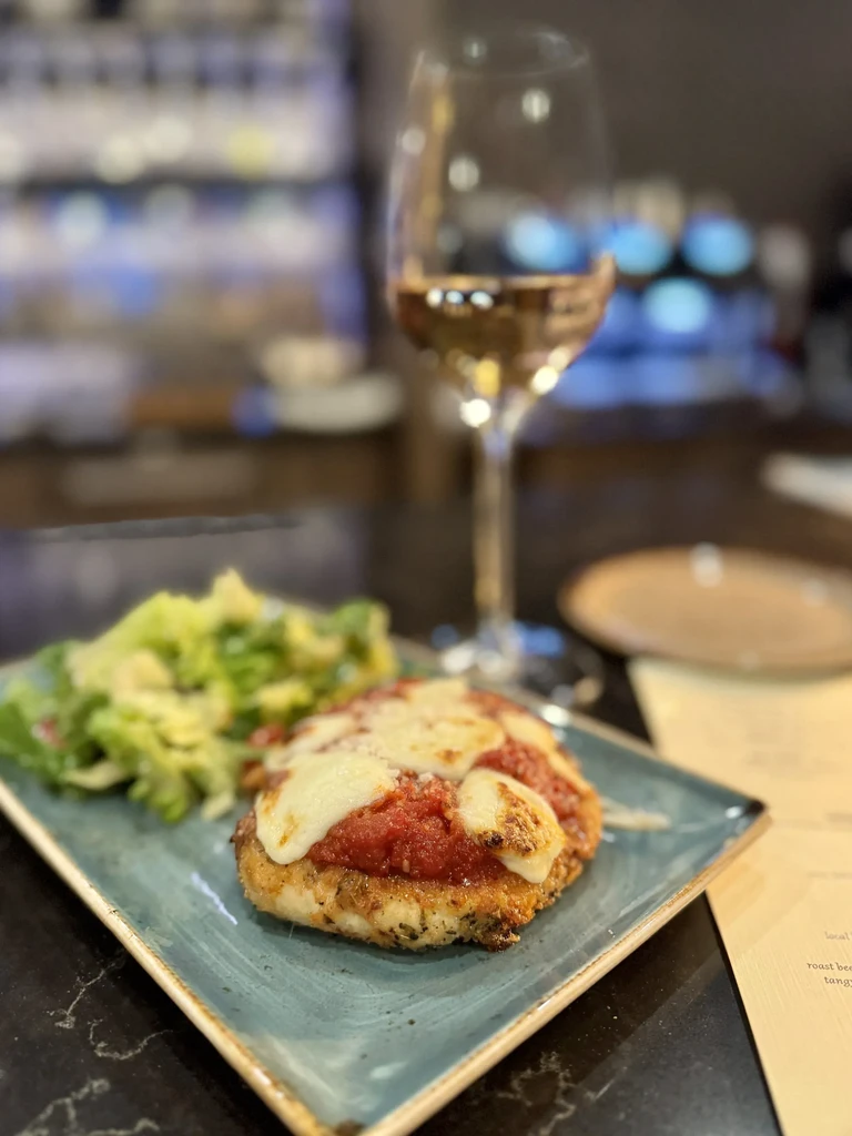 Chicken Parmesan, green salad, and rosé wine on a dark tabletop.