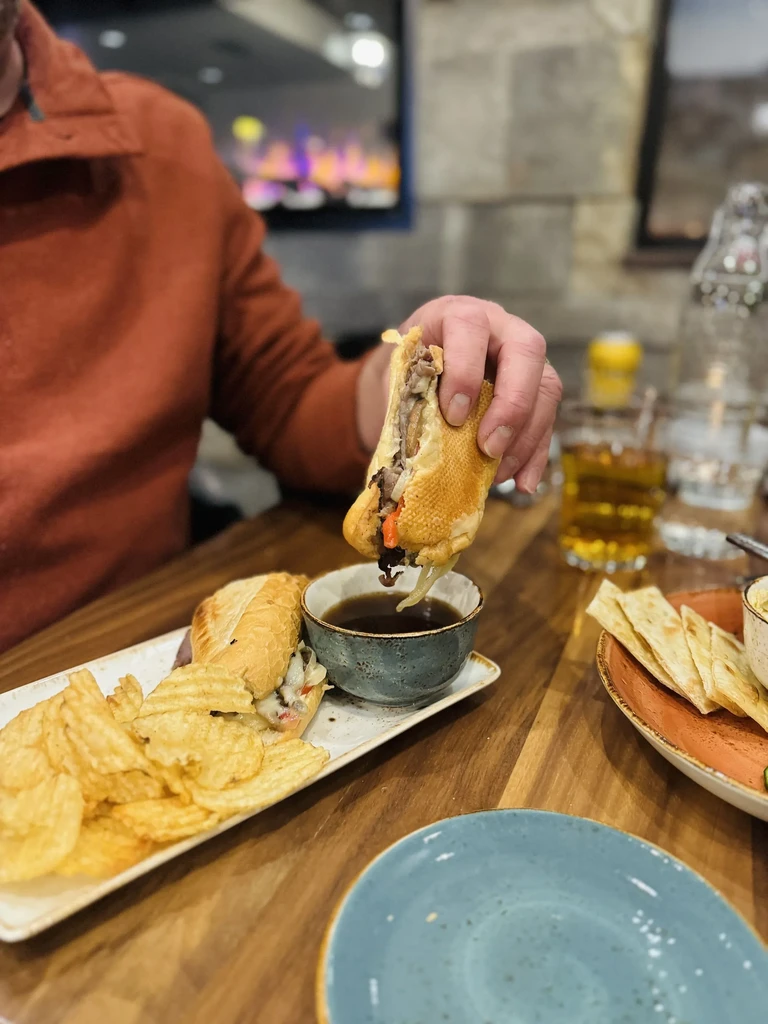 Close-up of hand holding French dip sandwich over au jus.