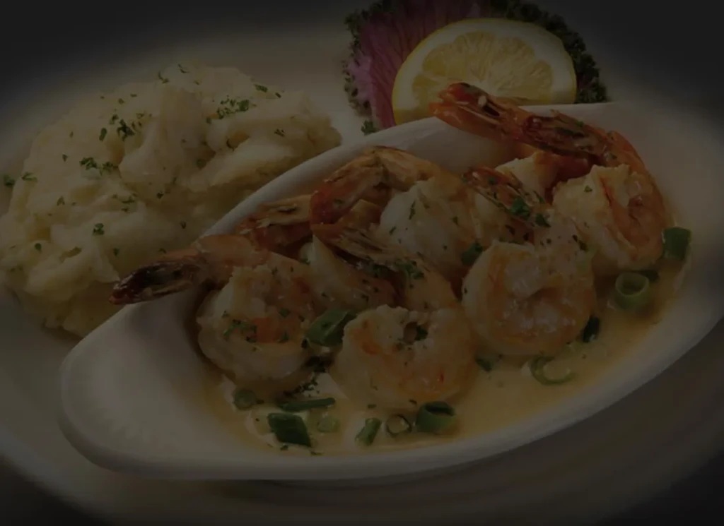 Plated creamy shrimp, mashed potatoes, lemon, and leafy greens.