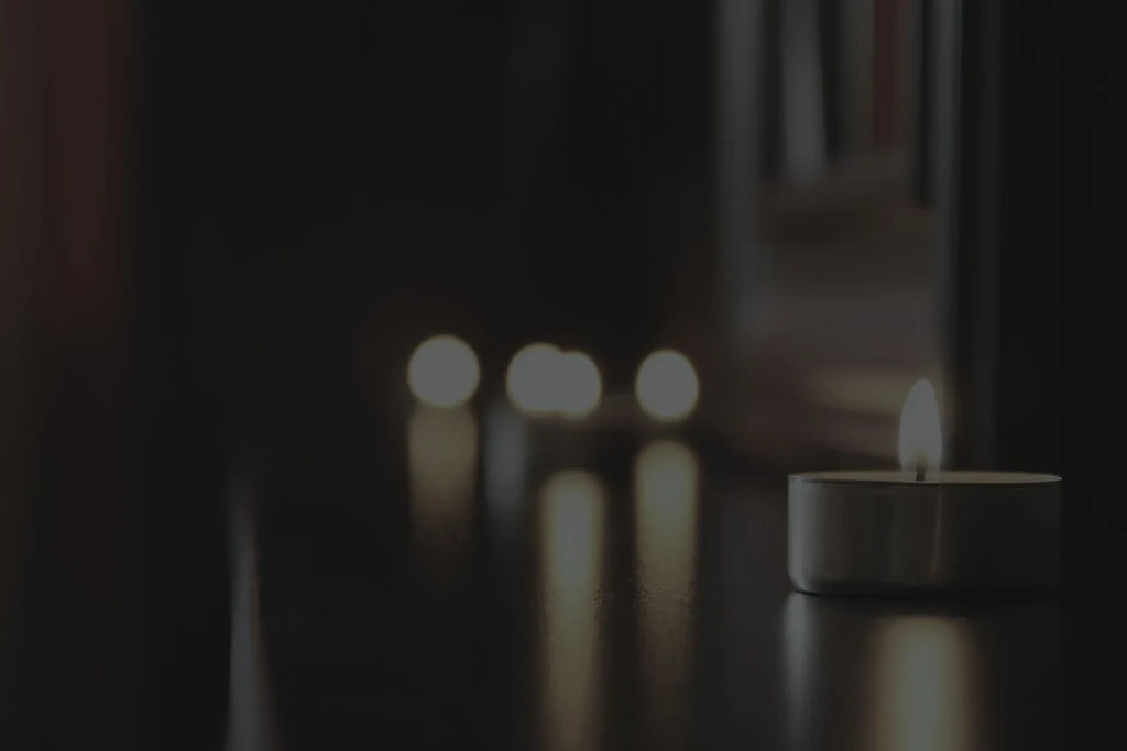 Lit tea light candle on dark surface with blurred background lights.