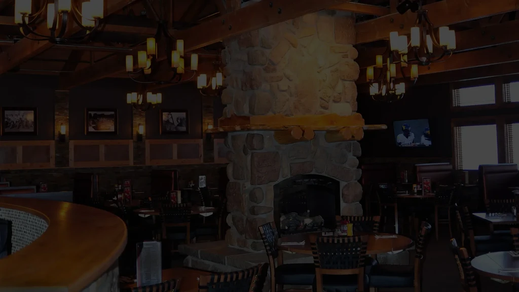 Restaurant interior: large stone fireplace, wooden beams, dim chandelier lighting.