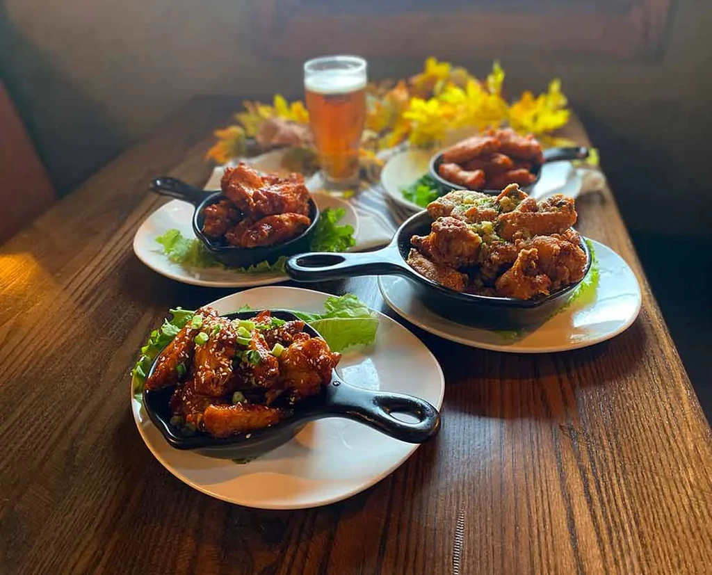 Multiple sauced chicken wings and a glass of beer on a dark table.