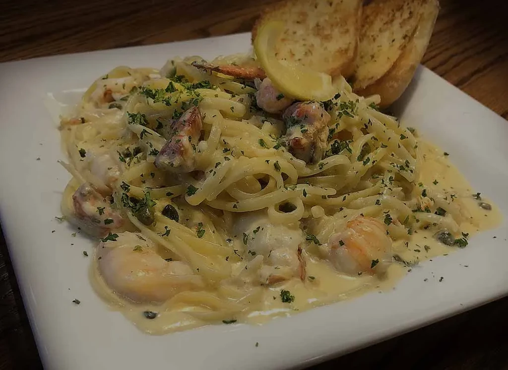 A plate of creamy seafood pasta with shrimp, lemon, and garlic bread.