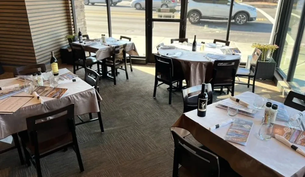 Empty restaurant dining room with set tables and street view windows.