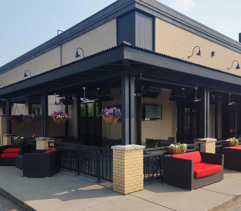 Modern restaurant building with shaded outdoor patio and red cushions.
