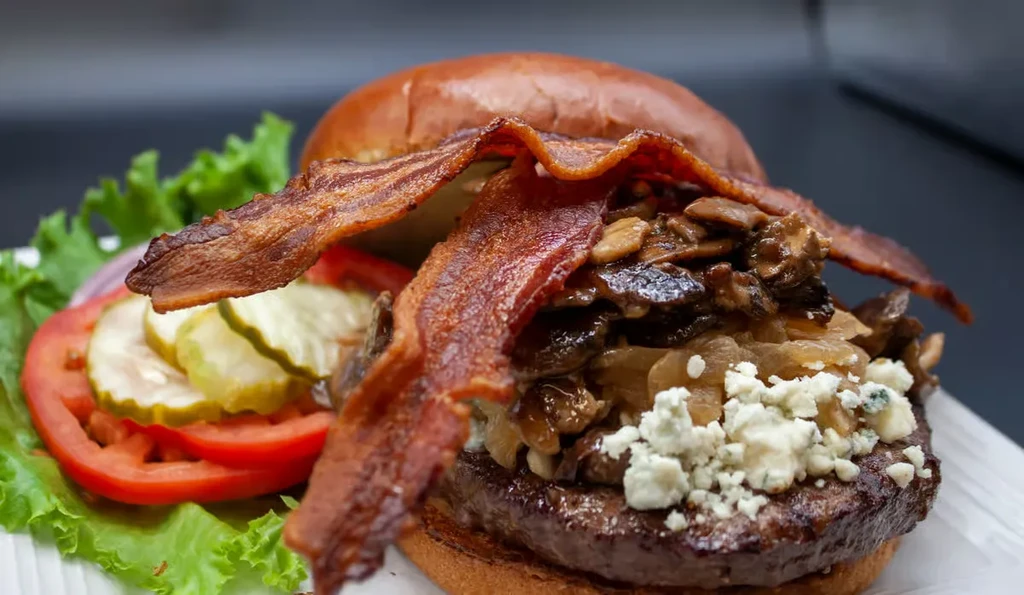 Beef burger with bacon, blue cheese, mushrooms, onions, lettuce, and pickles.