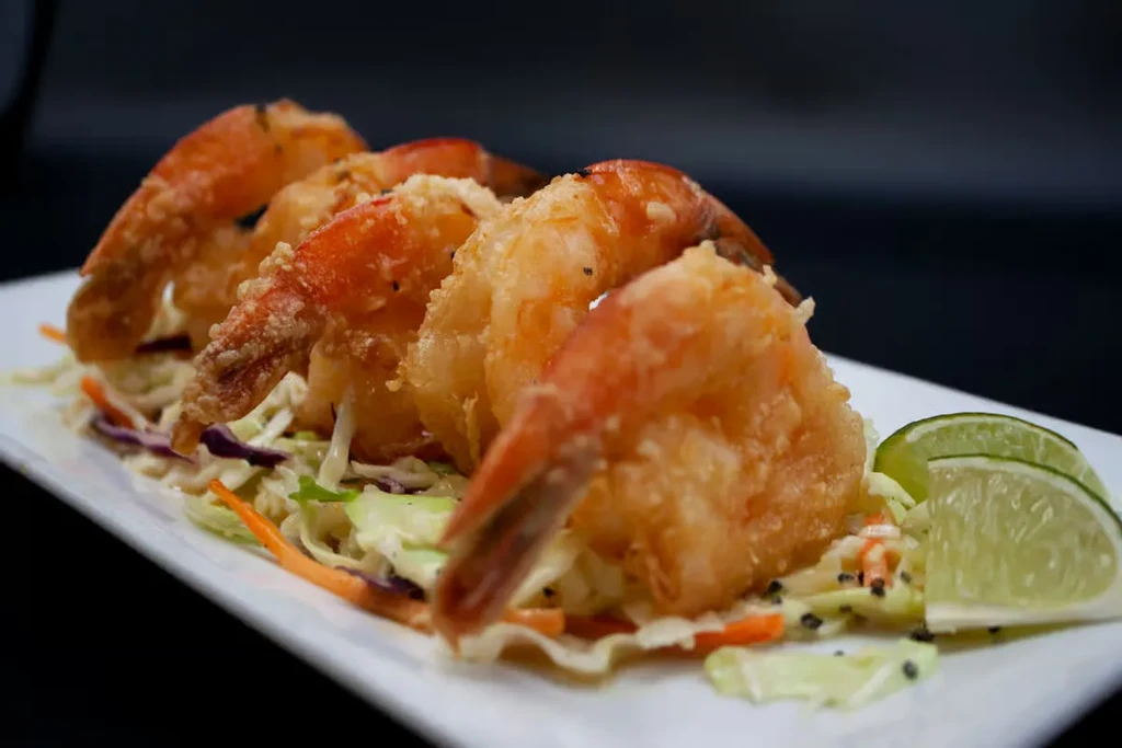 Five golden-brown fried shrimp with shredded vegetables and lime.