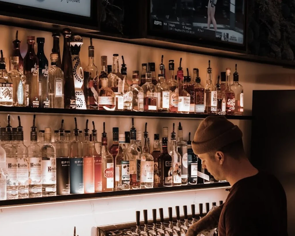 Well-stocked bar with illuminated liquor bottles and a bartender.