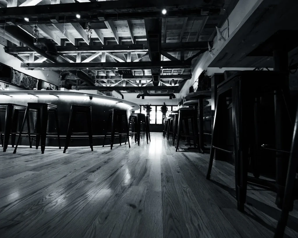 Black and white industrial bar interior, illuminated counter, exposed wooden beams.