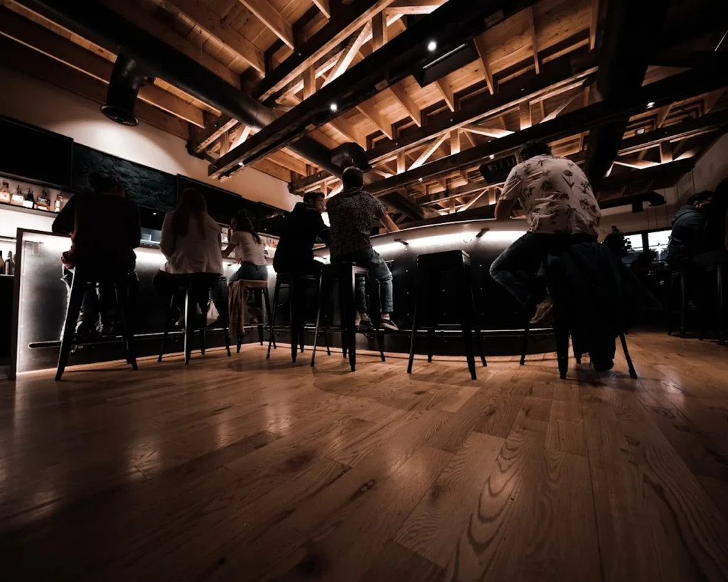Patrons at a sleek, dimly lit modern bar with exposed beams.