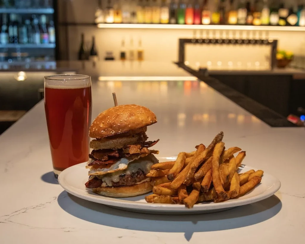 Stacked burger, french fries, and amber beer on a bar counter.