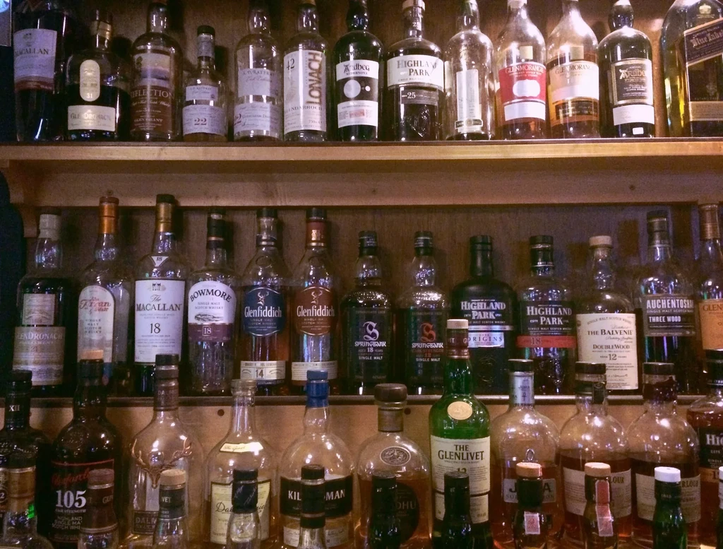 Three wooden shelves densely packed with various brands of whiskey bottles.