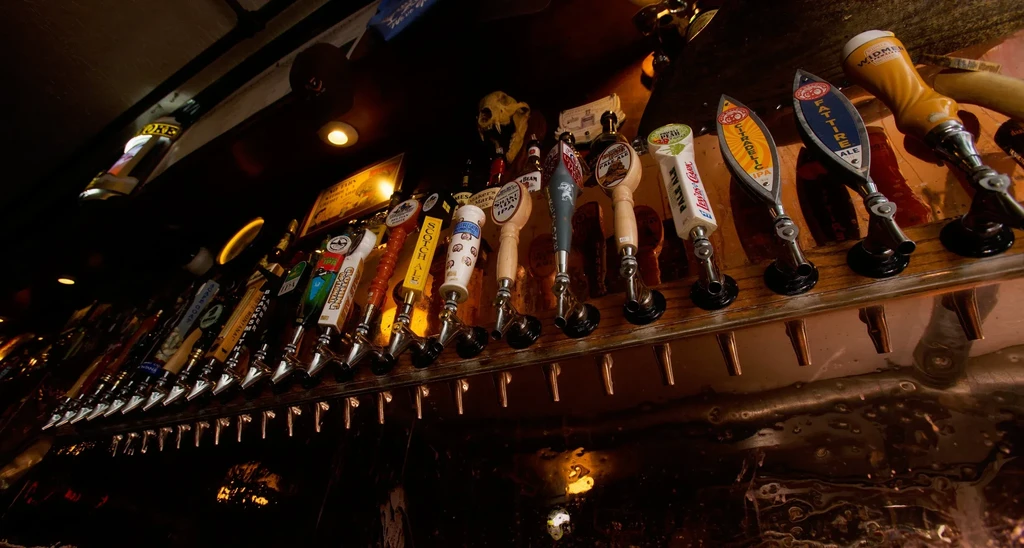 Numerous unique beer tap handles illuminated in a dark bar setting.