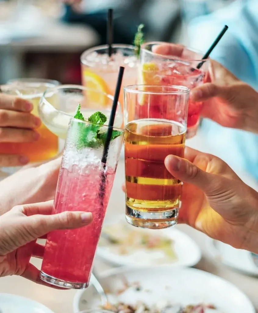 Close-up of hands toasting with various colorful beverages and food.