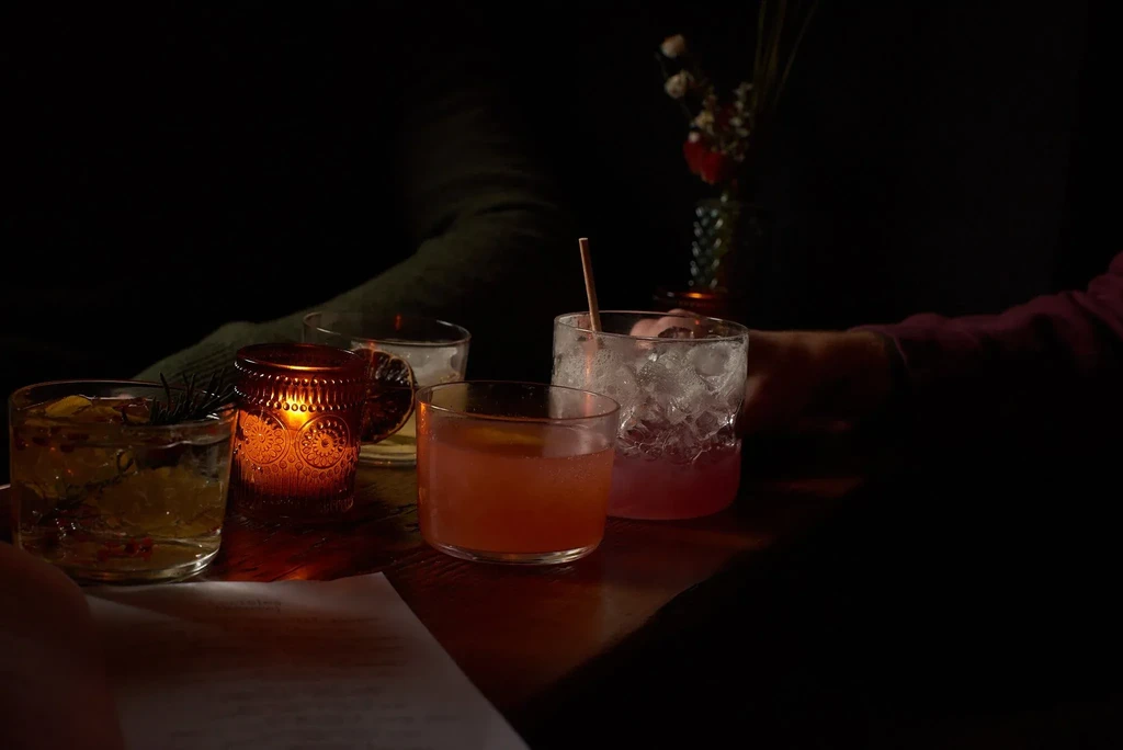 Three cocktails and a lit candle on a dimly lit table.