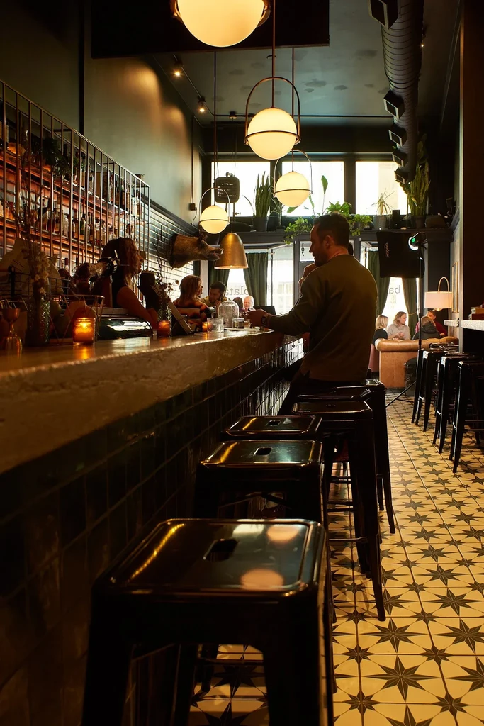 Warmly lit restaurant bar with patrons and unique patterned floor.