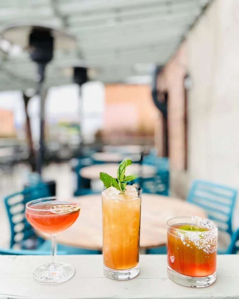Three colorful, garnished cocktails on an outdoor patio table.