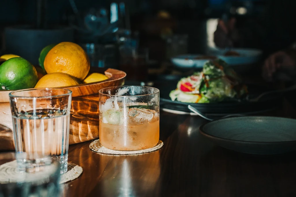 Drinks, citrus fruit, and fresh salad on a dim restaurant table.