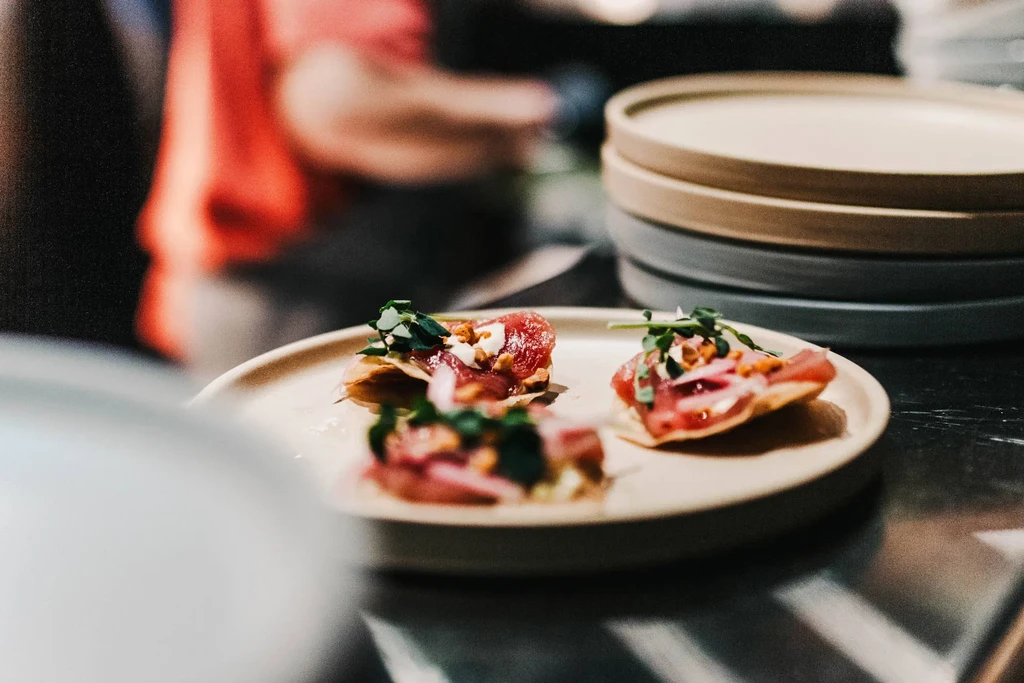 Close-up of three appetizers with raw fish, white sauce, and microgreens.