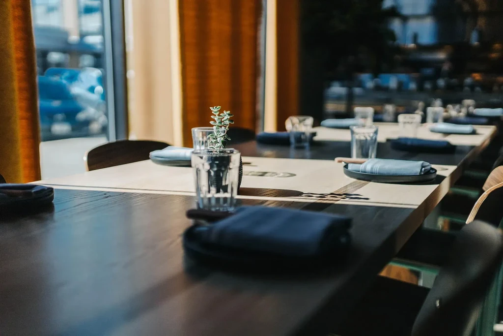 Empty modern restaurant with a long, meticulously set wooden dining table.