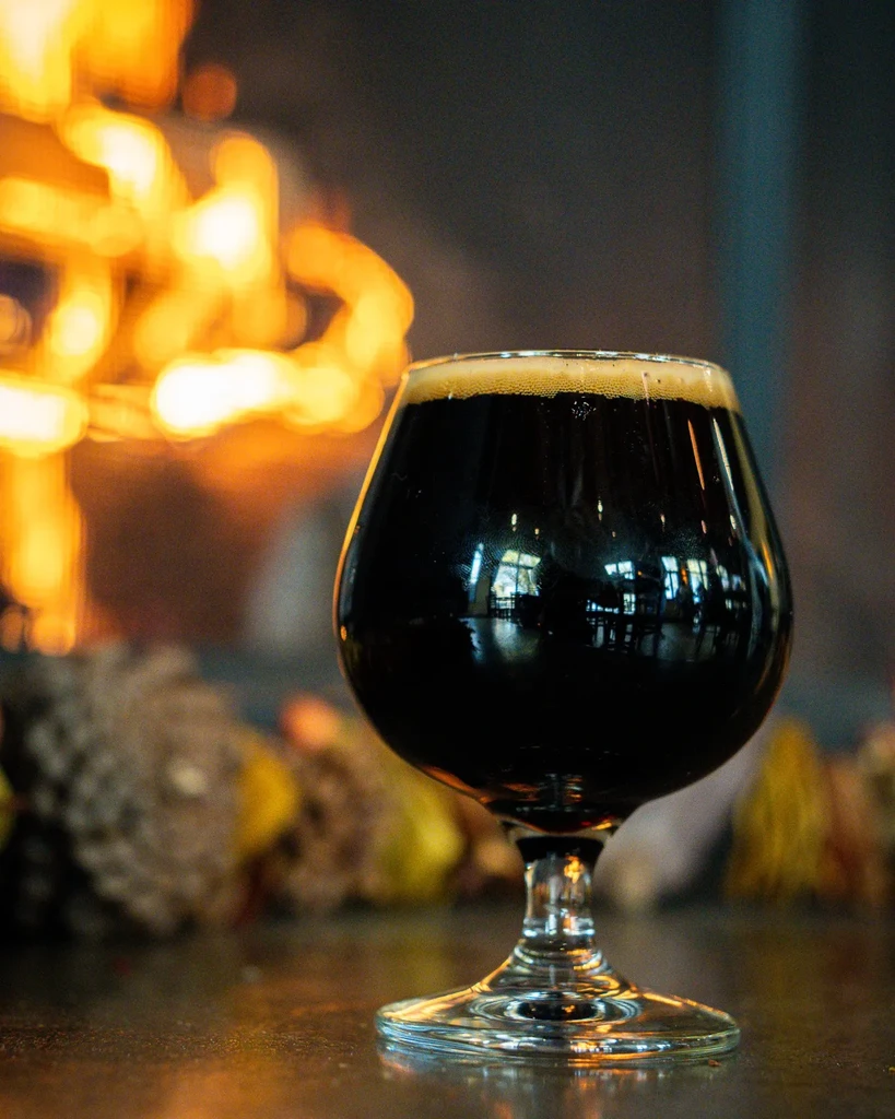 Dark beer with creamy foam in tulip glass, blurred warm background.