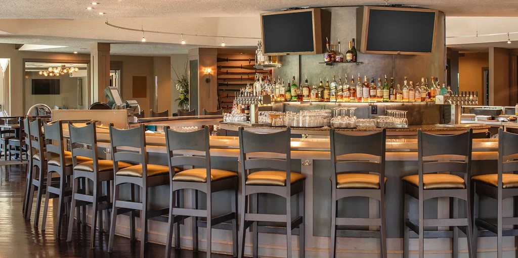 Circular bar with illuminated liquor bottles, empty stools, and rifle display.