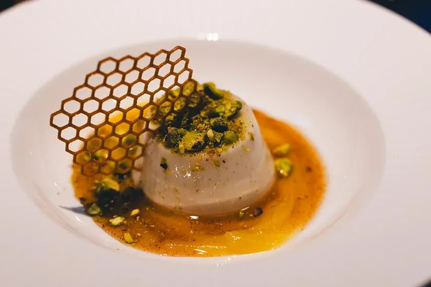 Plated dome dessert with pistachios, orange sauce, and a lattice crisp.