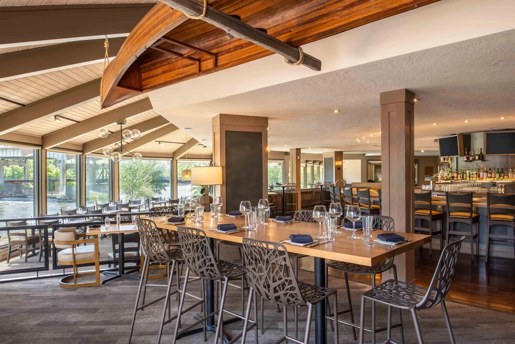 Empty modern restaurant interior with dining, bar, river view, and suspended canoe.