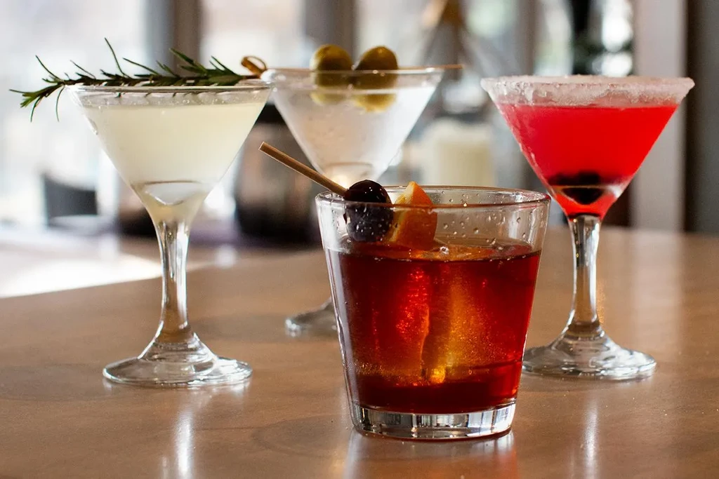 Four distinct, colorful cocktails with different garnishes on a table.