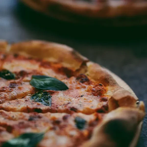 Close-up pizza with golden crust, melted cheese, red sauce, and basil.