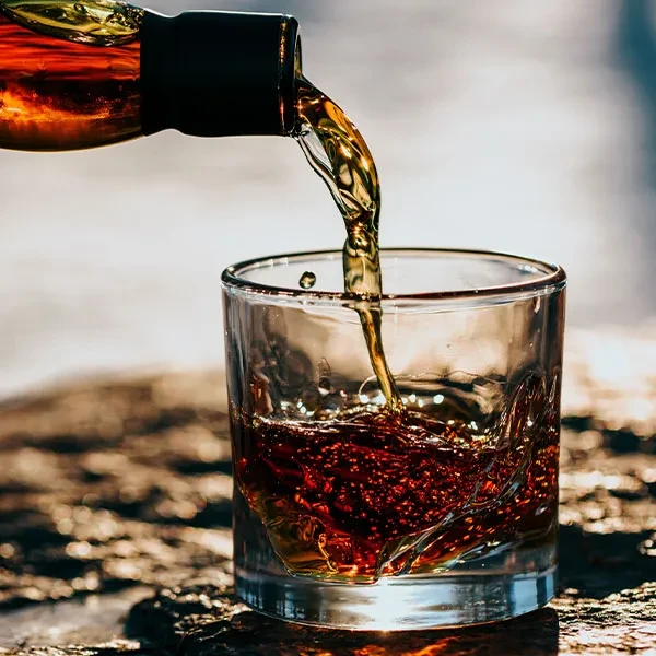 Amber liquid pours from bottle into textured glass, splashing.