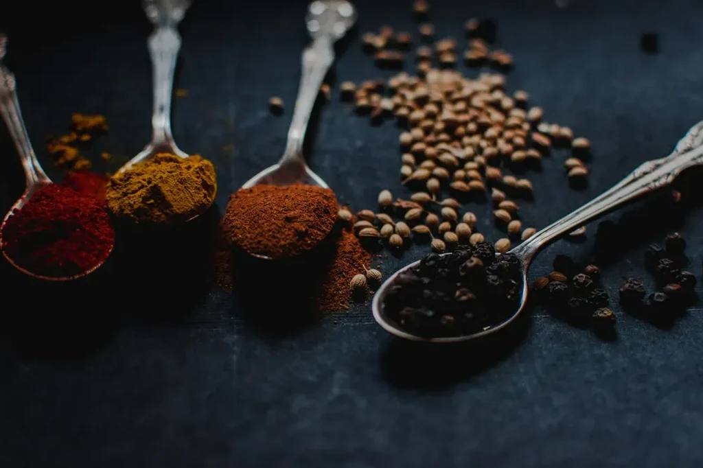 Antique silver spoons hold various colorful spices and coriander seeds.