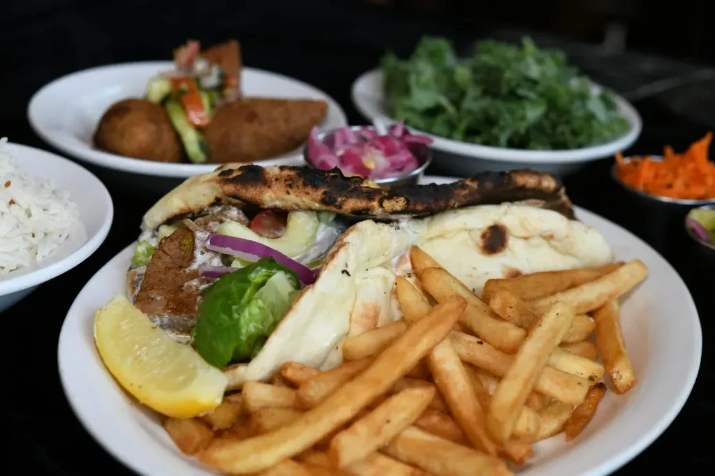 Grilled meat flatbread, french fries, lemon, and Middle Eastern side dishes.