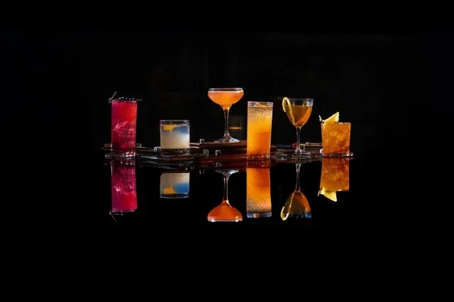 Assorted cocktails with vibrant colors and garnishes on a reflective black surface.