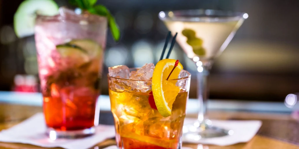 Three distinct cocktails with various garnishes on a bar.