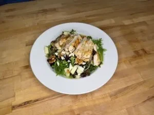 Grilled chicken salad with crumbled cheese, green fruit, on wood.