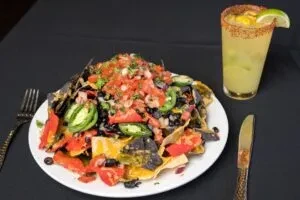 Plate of vibrant nachos and a chili-rimmed drink with a lime.