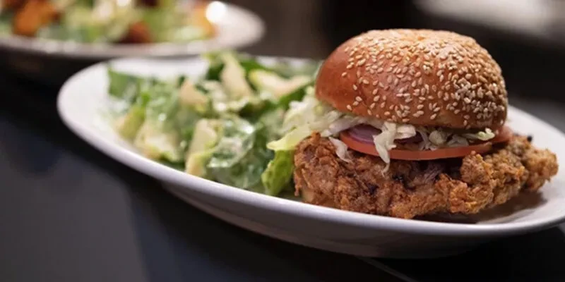 Crispy fried chicken sandwich with lettuce, tomato, onion, and Caesar salad.