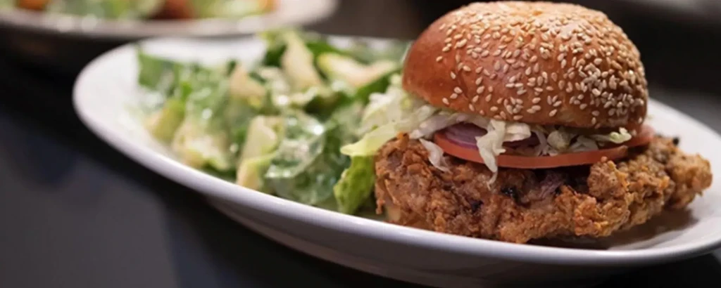 Fried chicken sandwich, tomato, lettuce, onion, and side salad.