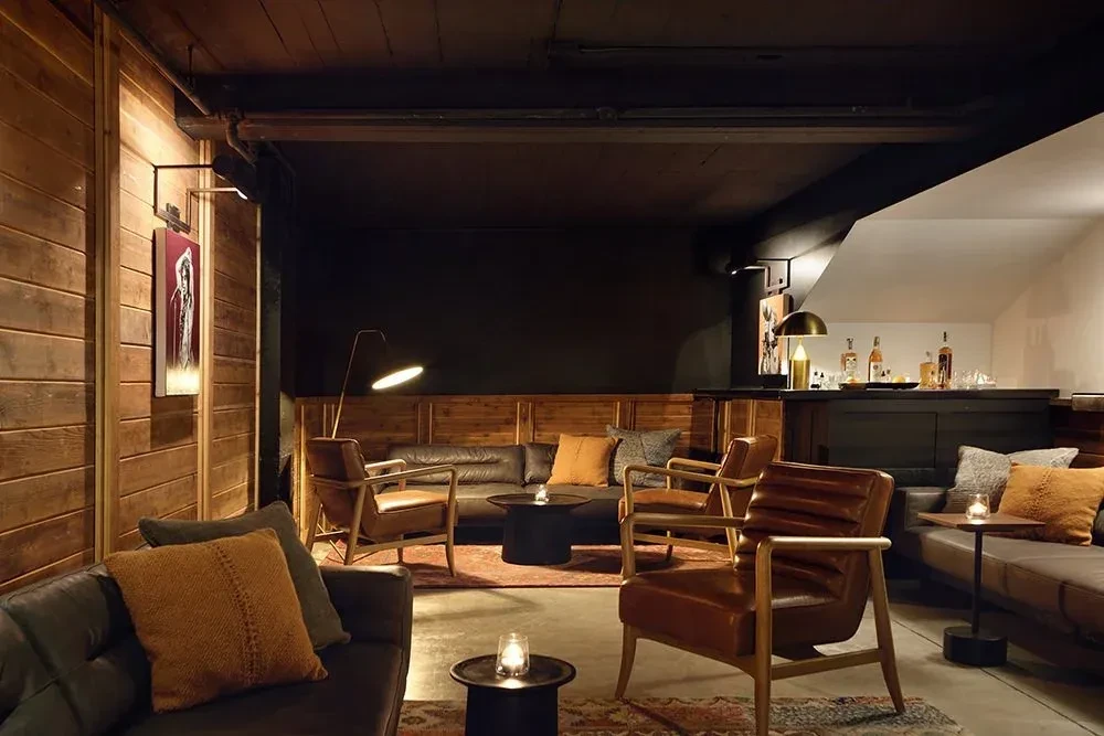 Cozy, sophisticated restaurant lounge with dark leather sofas, wooden walls, and dim lighting.