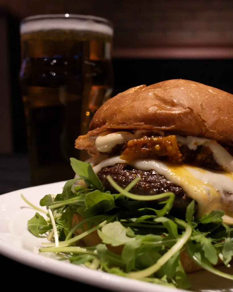 Gourmet burger with brioche bun, melted cheese, arugula, and beer.