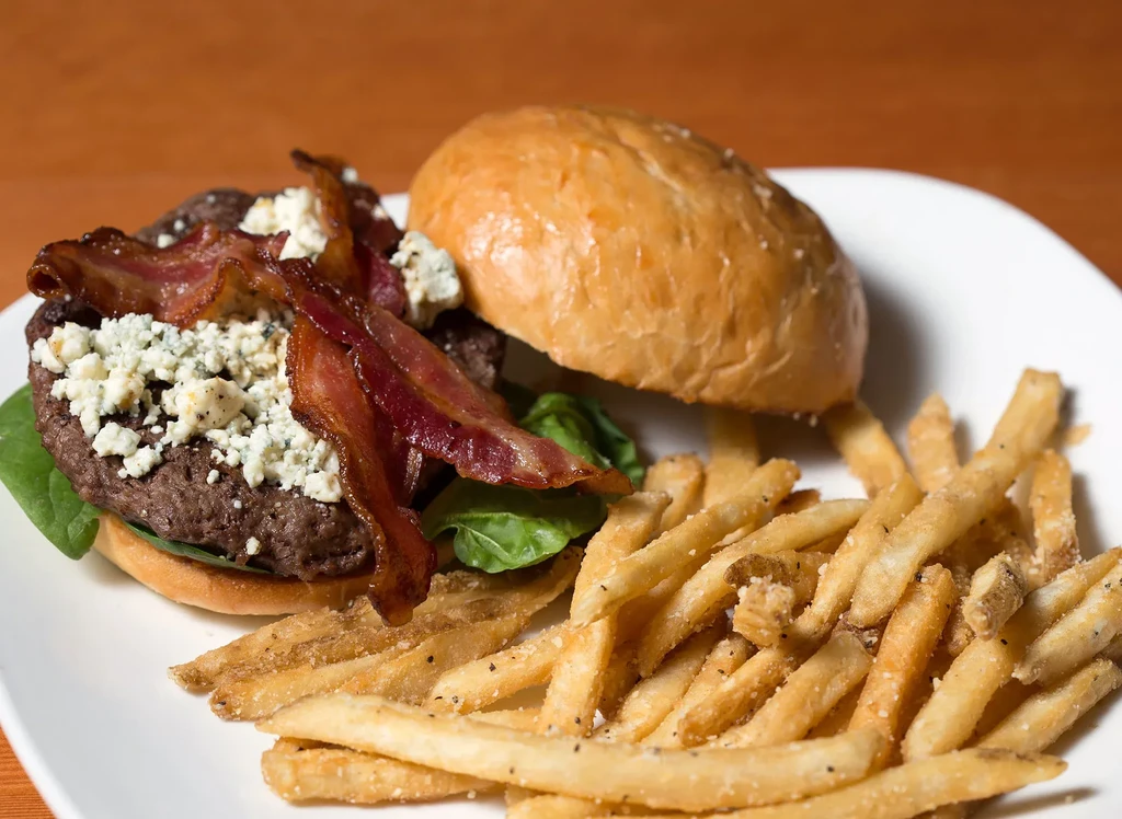 Burger with blue cheese, bacon, greens, and a side of fries.