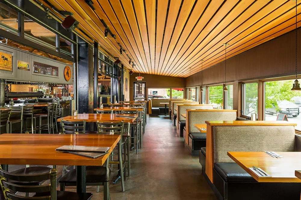 Well-lit restaurant interior featuring a bar, dining tables, and window booths.