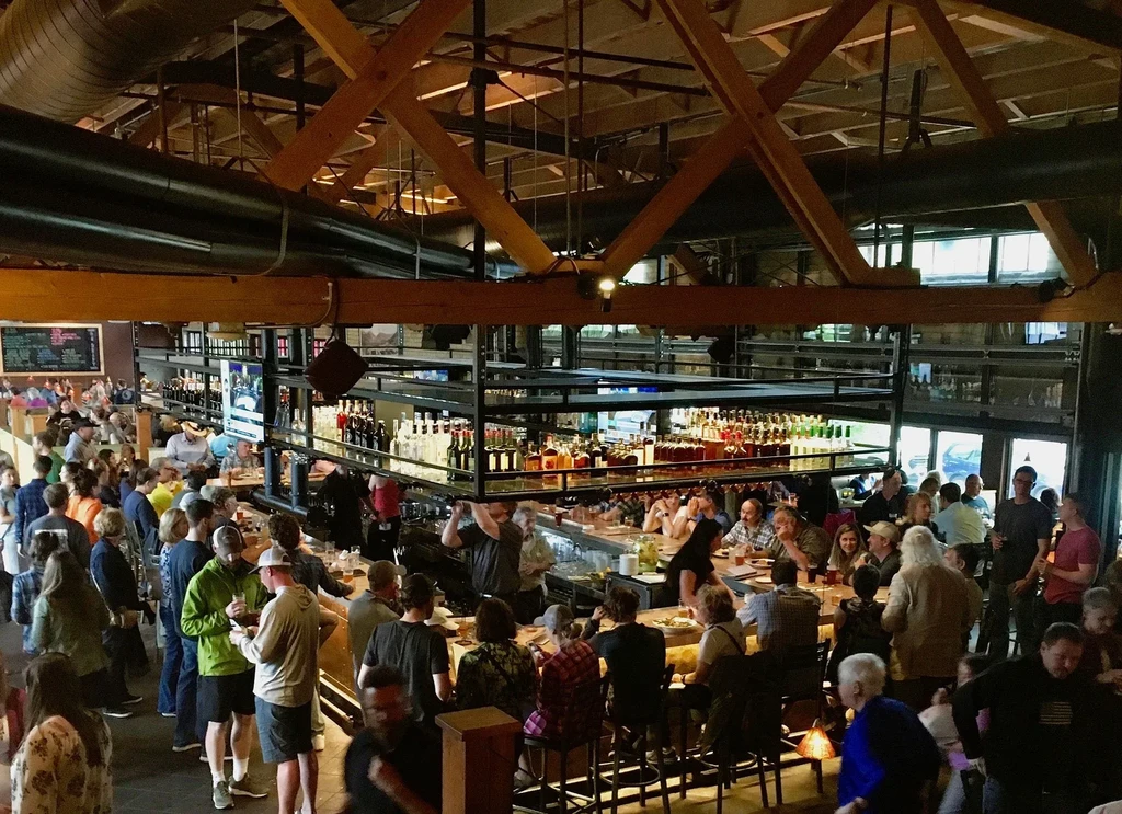 Crowded industrial-chic bar with extensive liquor bottles and active patrons.