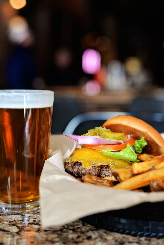 Cheeseburger, fries, and beer in a basket on a marble counter.