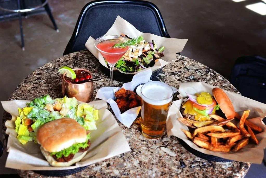 Gastropub table spread with burgers, salads, fries, and drinks.