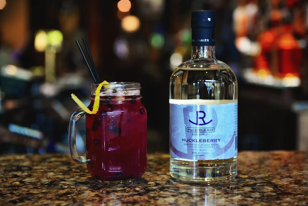 Reddish-purple huckleberry cocktail and Rocking R Bar spirits bottle.