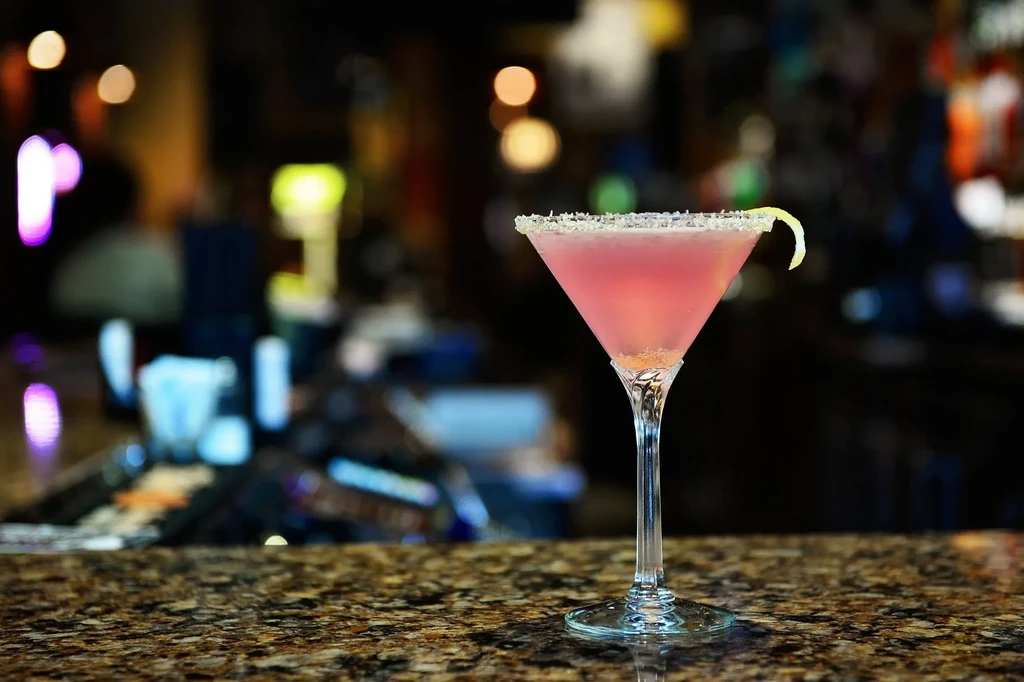 Pink martini cocktail with a citrus twist at a bar.