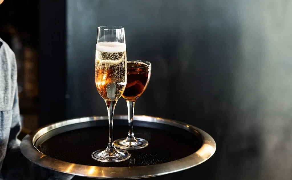 Person holding tray with champagne and a dark spirit.