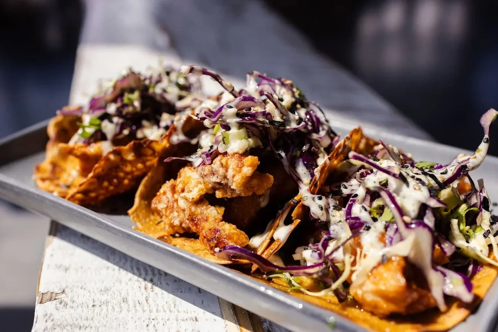Three crispy tacos with purple cabbage and white sauce on a tray.
